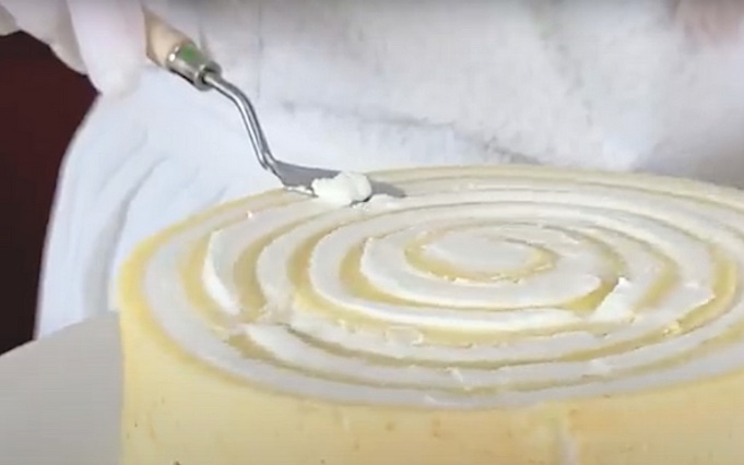 Кондитерским шпателем снимите излишки крема сверху торта.