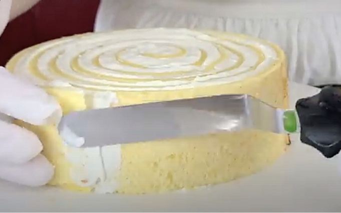 Небольшим количеством крема обмажьте торт с боков и шпателем выровняйте слой крема